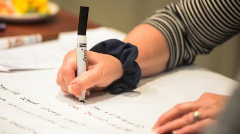 A woman's hand holding a pen writing on a large piece of paper.